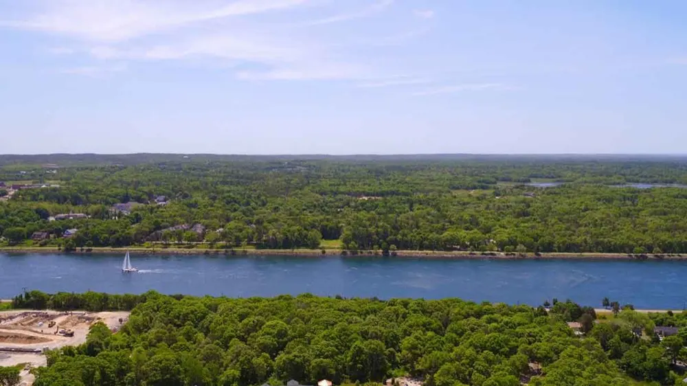 A sailboat on the Cape Cod Canal framed by green shoreline