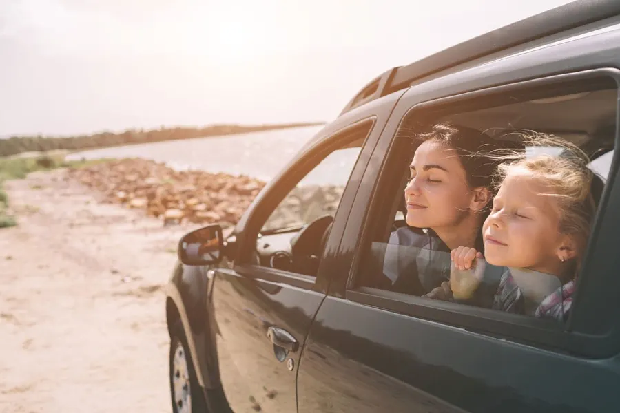A mother and daughter looking out the window of an SUV beside the water
