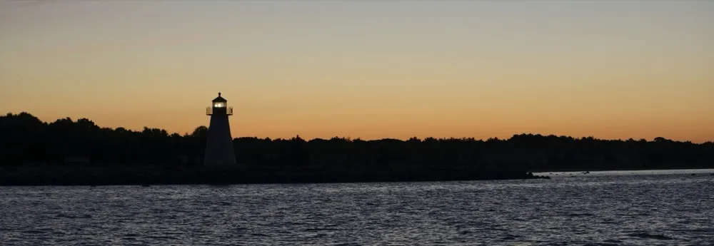 A lighthouse silhouetted against an orange sunset over the water